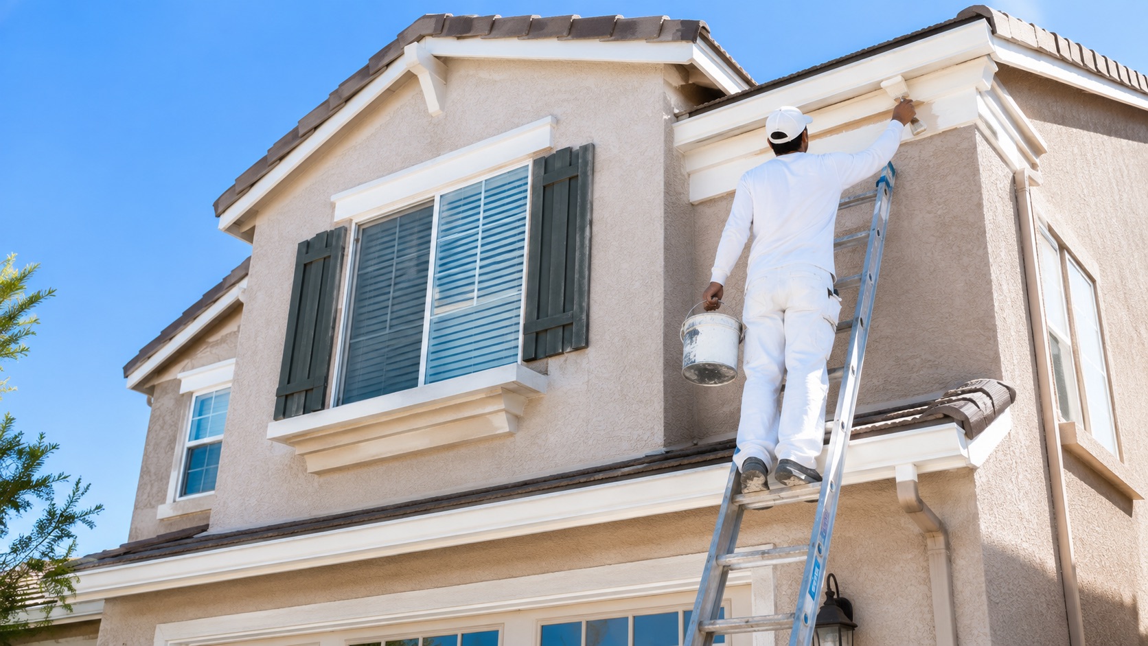 Exterior painting in progress on a stucco home in Tracy CA, painter on ladder